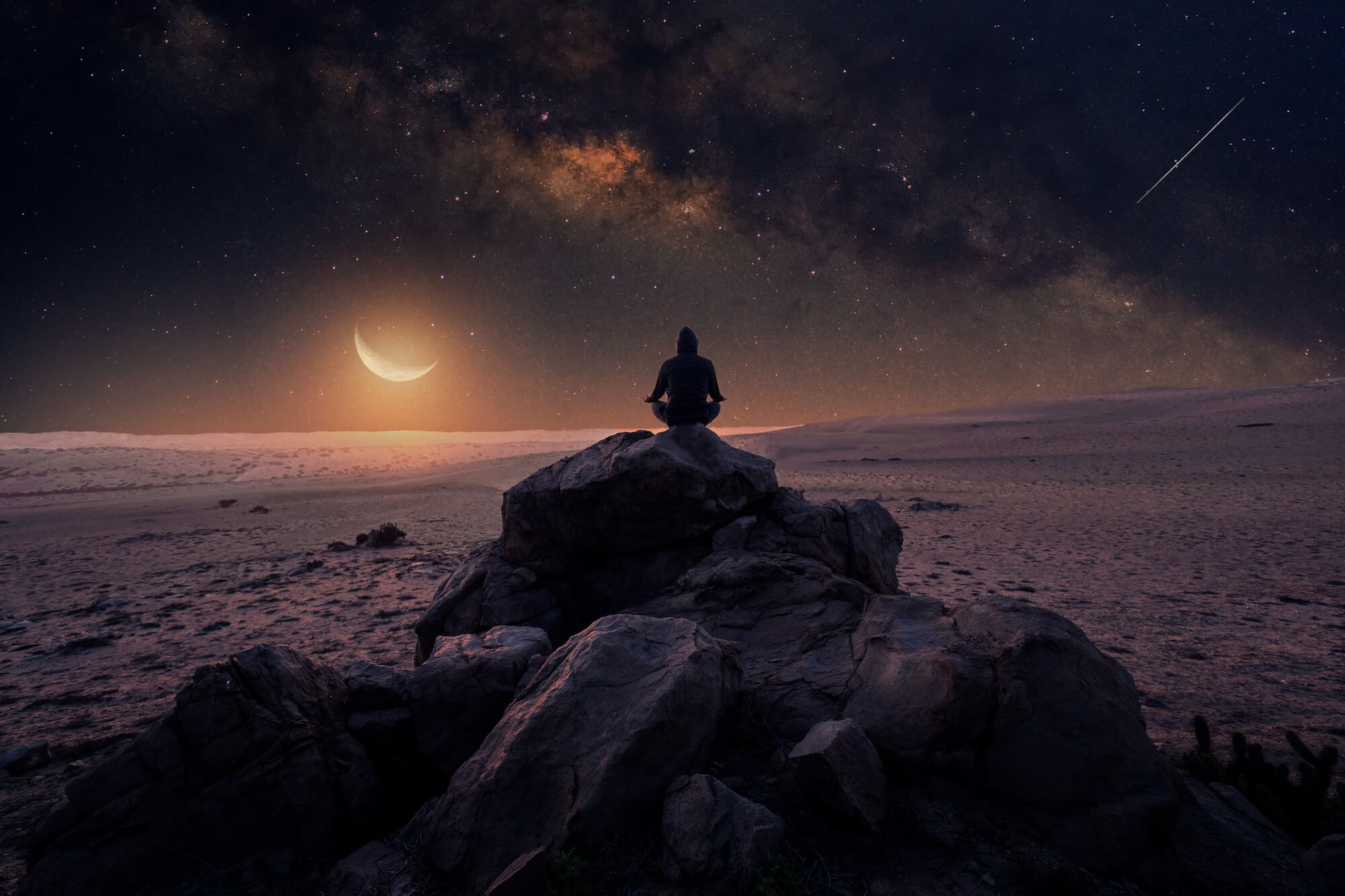 Ein Mann meditiert auf einem Felsen unter dem Sternenhimmel.