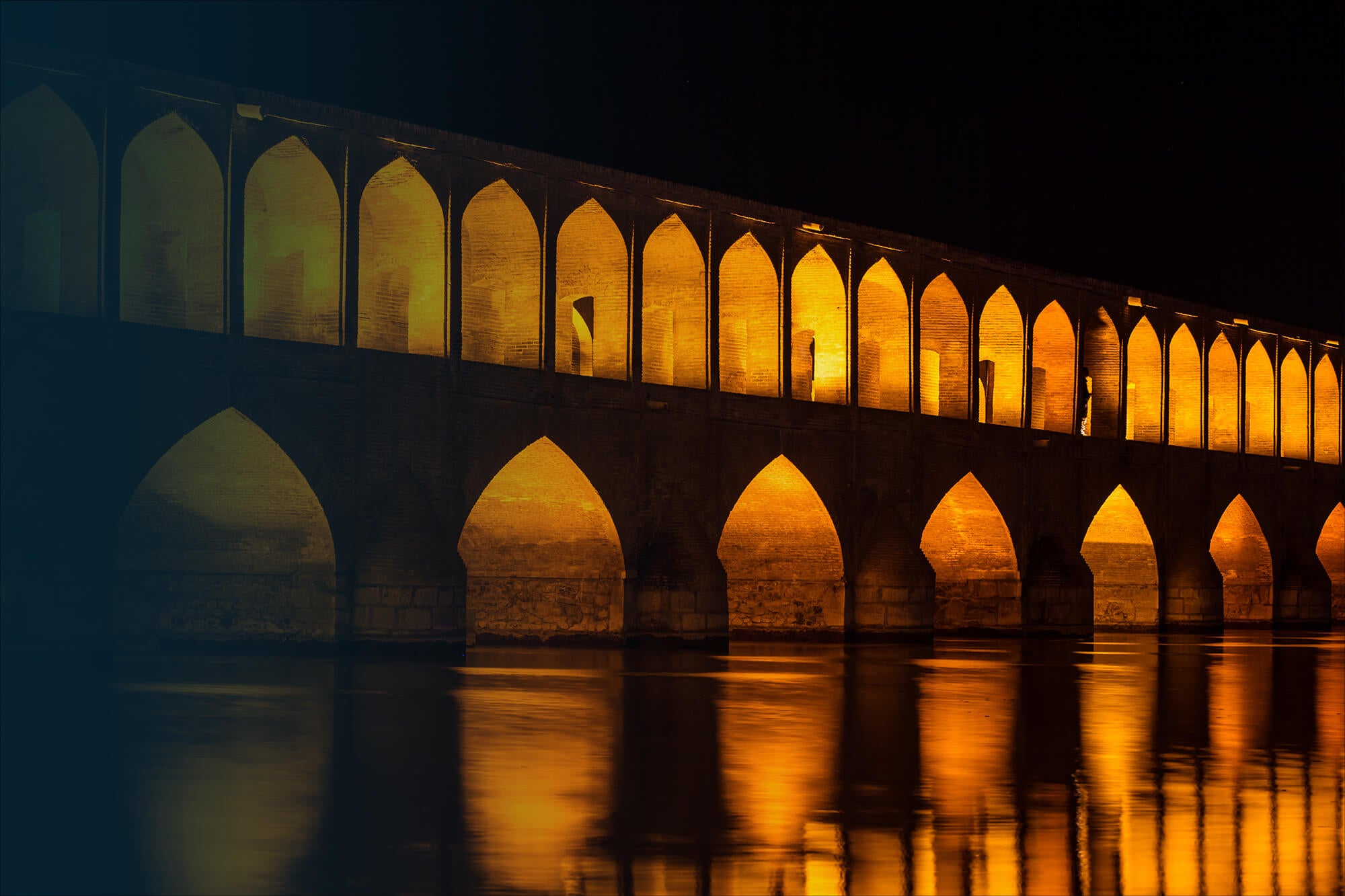 Ein Bild von der 33-Säulenbrücke in Isfahan bei Nacht. Die Brücke ist angeleuchtet.