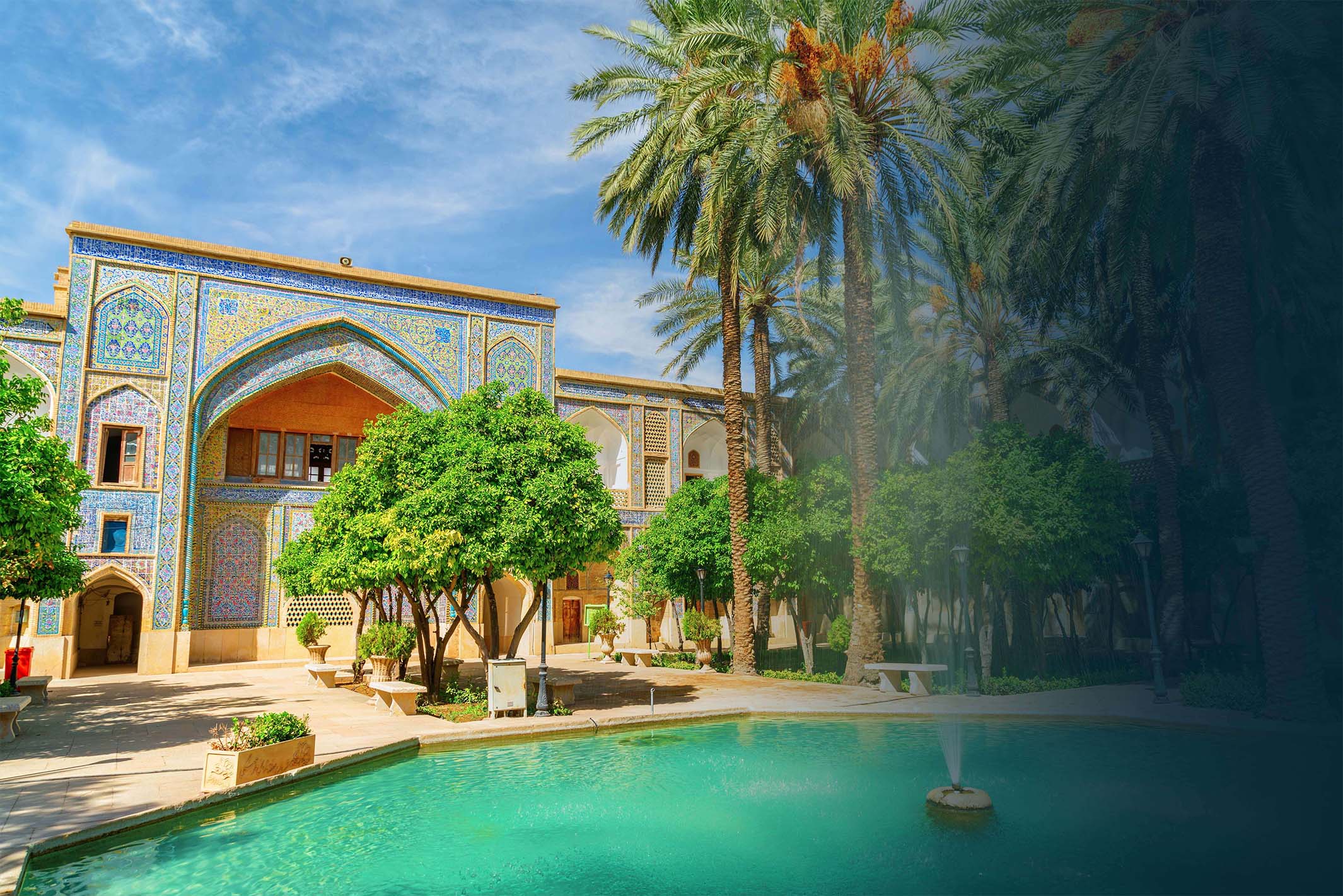 Ein Bild von einer persischen Villa, umgeben von einem Teich und vielen Palmen.